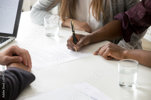 African american man puts signature on contract, interracial couple buying insurance or taking bank loan, making financial deal, family customers signing prenuptial agreement concept, close up view