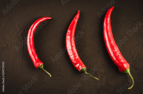 Three red Chile pepper on a dark background/Three red hot Chile pepper on a dark stone background. Top view