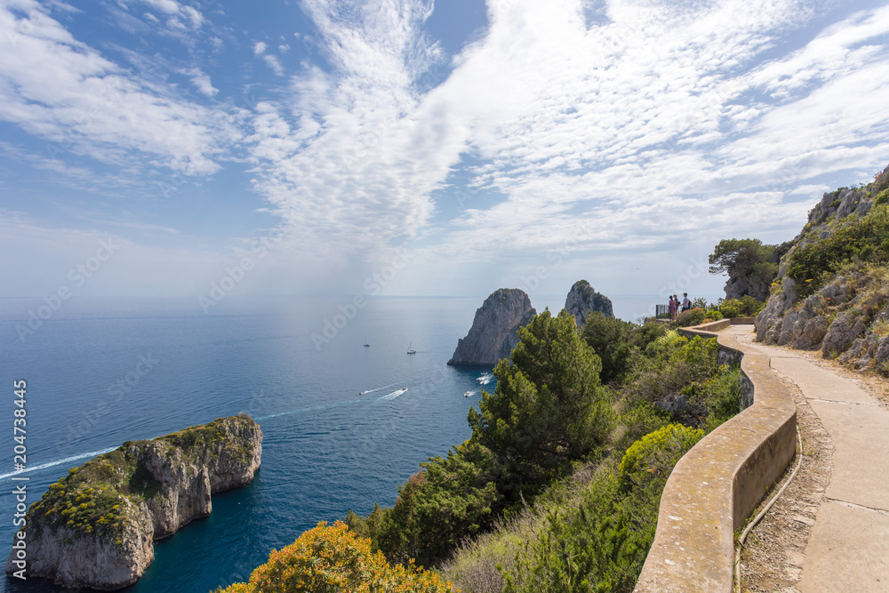 Capri Italy, island in a beautiful summer day, with faraglioni rocks and boat crossing the bay.