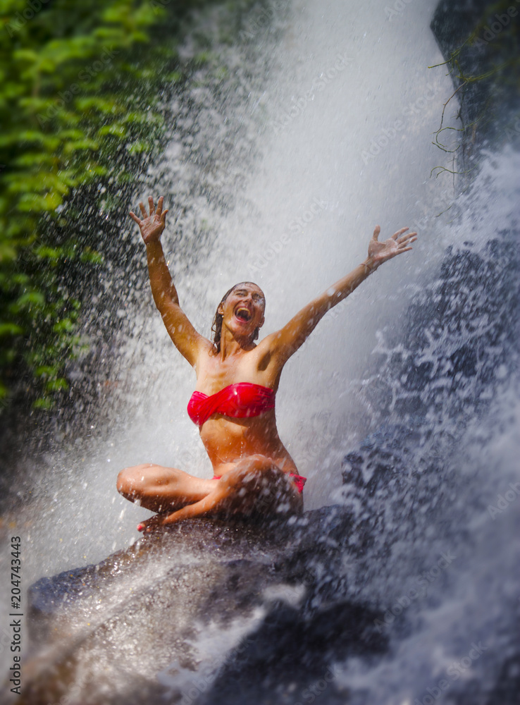 Fototapeta premium young attractive and happy woman with fit body practicing yoga wet under tropical paradise waterfall stream screaming excited with opened arms