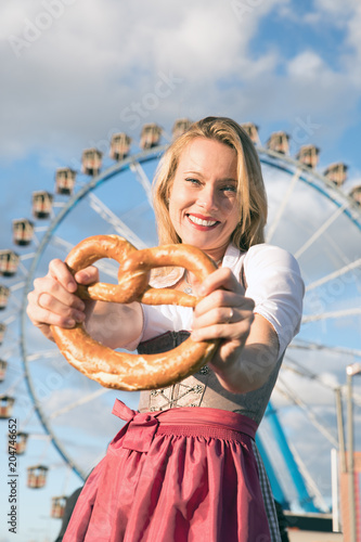 young sexy woman is doing oktoberfest in munic summer, spring folk festival she is wearing a dirndl and holding a hear brezn in her hand