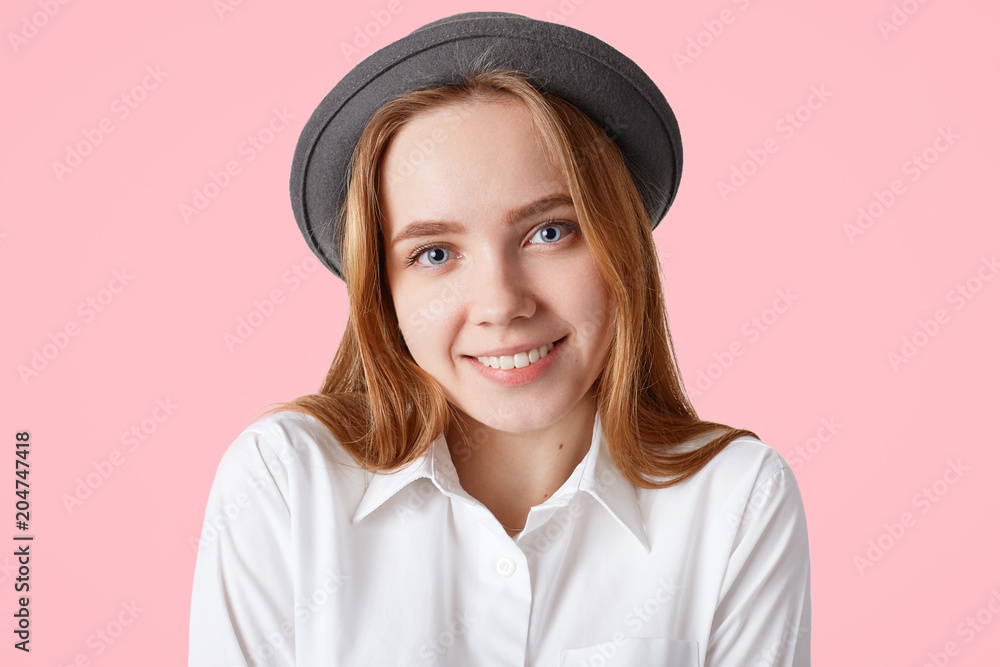 Headshot of pleased female has healthy skin, pleasant smile on face, wears elegant black hat, isolated on pink studio background. Lovely woman expresses positive emotions, models indoor alone Headshot of pleased female has healthy skin, pleasant smile on face, wears elegant black hat, isolated on pink studio background. Lovely woman expresses positive emotions, models indoor alone