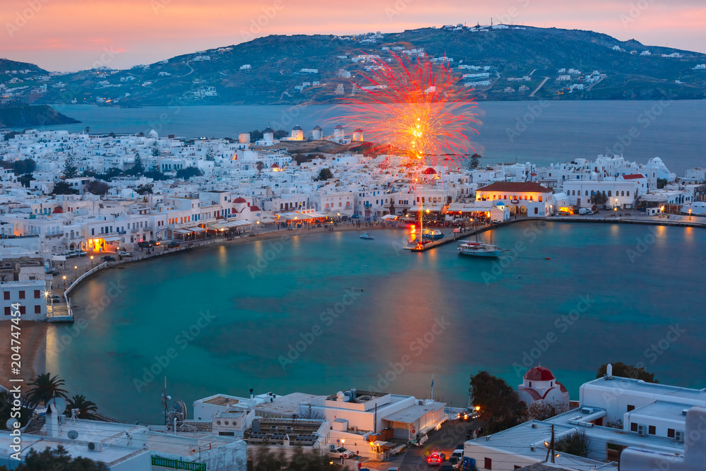 Aerial view of Mykonos City, Chora with Old Port, white houses, windmilles and churches on the island Mykonos, The island of the winds, during evening blue hour, Greece