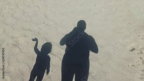 Shadow of a man and a kid on sandy background, waving