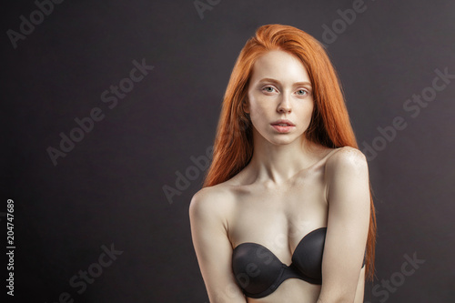 Slim young girl with long gorgeous red hair and strapless bra on black background with copyspace . Healthy Hair and Skin Care photo