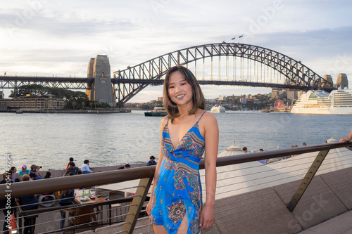 Young woman in blue dress standing in front of Sydney Harbour Bridge