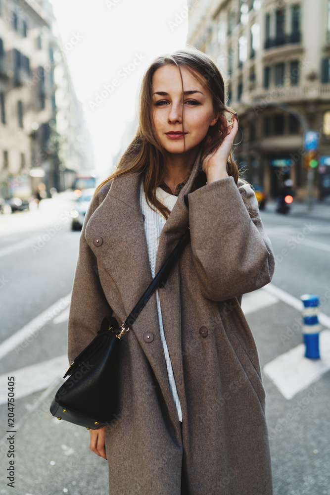 International student girl in stylish clothes walking the street on a weekend day. Tourist female exploring the city during one-day journey on a warm sunny day. Hipster girl in oversized coat outdoors