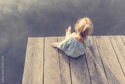 Lonely small girl sitting near river. Riskily situation photo