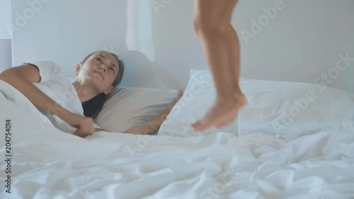 Little girl jumping on bed and wakes up her young mother in the early morning