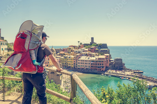 Active father carrying his child in backpack looking at sea town.