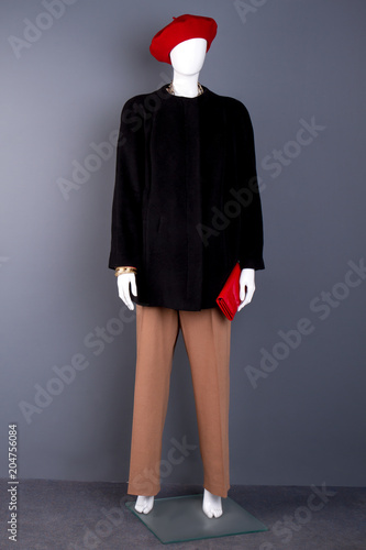 Female mannequin with red beret and wallet. Full length dummy in fashion coat and trousers, grey background. Ladies fashion look.