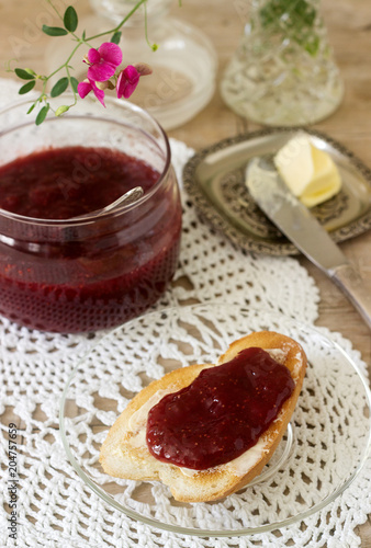Strawberry jam in a glass jar and toast with butter and jam. Rustic style.