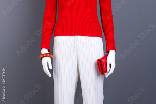 Mannequin with red sweater, bracelet and wallet. Red pullover and white trousers for women. Feminine stylish garment and accessories.