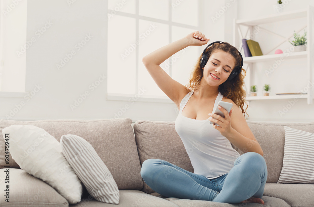 Happy young woman in headphones on beige couch Happy young woman in headphones on beige couch