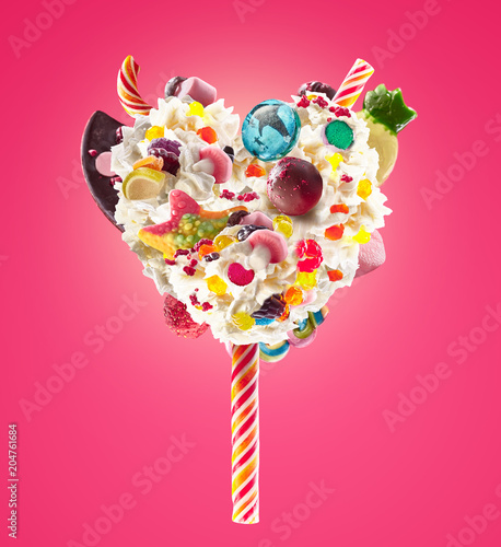 Sweet Lolipop in Heart form of whipped cream with sweets, jellies, heart front view. Crazy freakshake food trend. Front view of whipped heart of cream lolly, full of berry and jelly sweets, chocolate photo