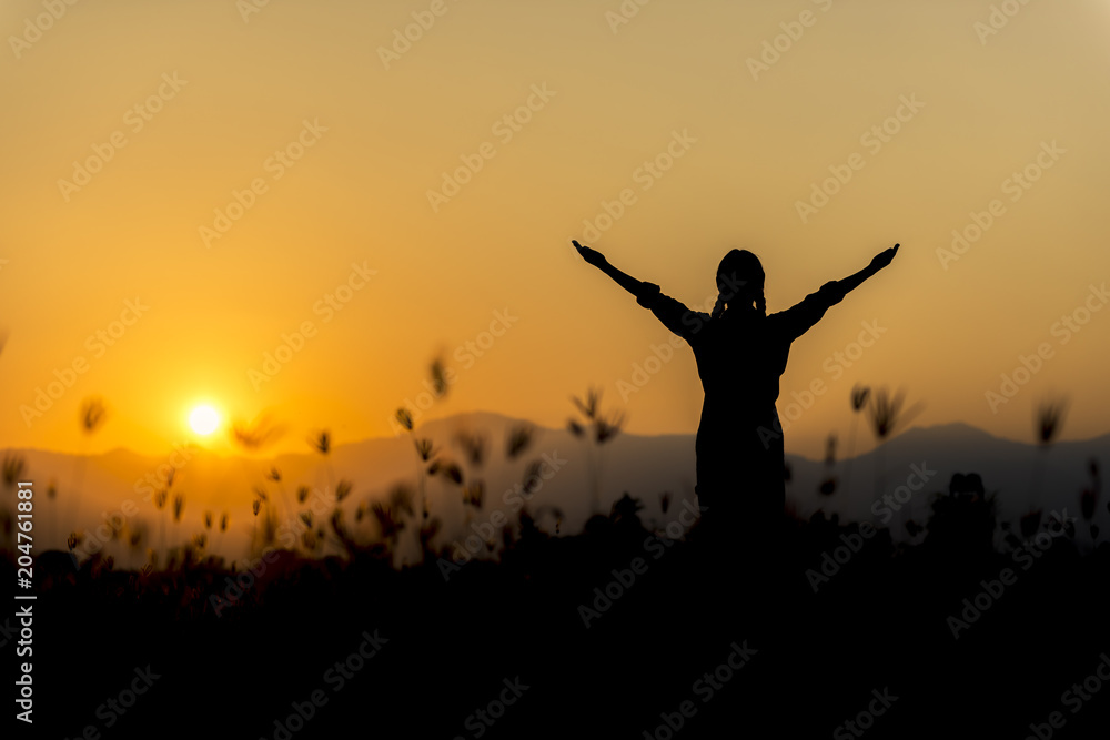 Silhouette woman at sunset standing elated with arms raised up above her head.