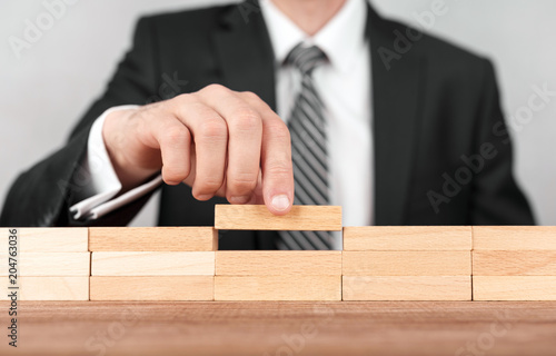 Close-up of businessman completing building wall of wooden bricks on table, copy space.
