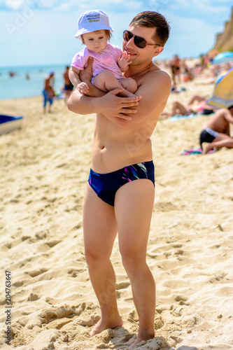 Young father in sunglasses on the beach with a little daughter