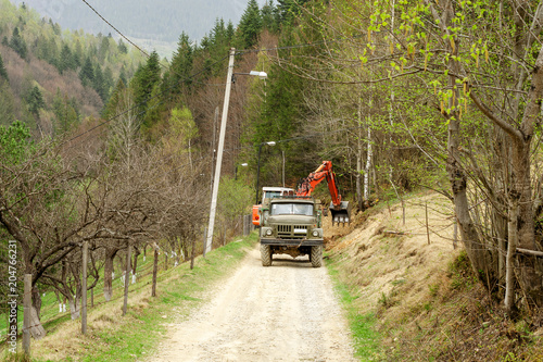 The excavator expands the road and loads the land in a truck in the mountains of the Carpathians, Ukraine. Outdoors.