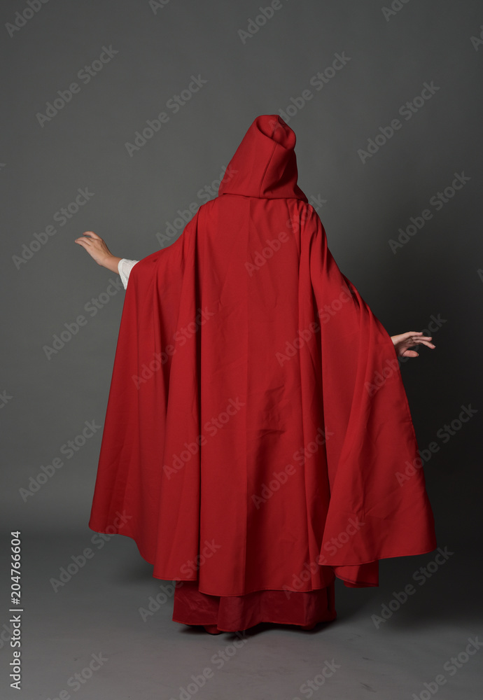 full length portrait of woman wearing red fantasy costume with cloak, standing pose on grey studio background. full length portrait of woman wearing red fantasy costume with cloak, standing pose on grey studio background.