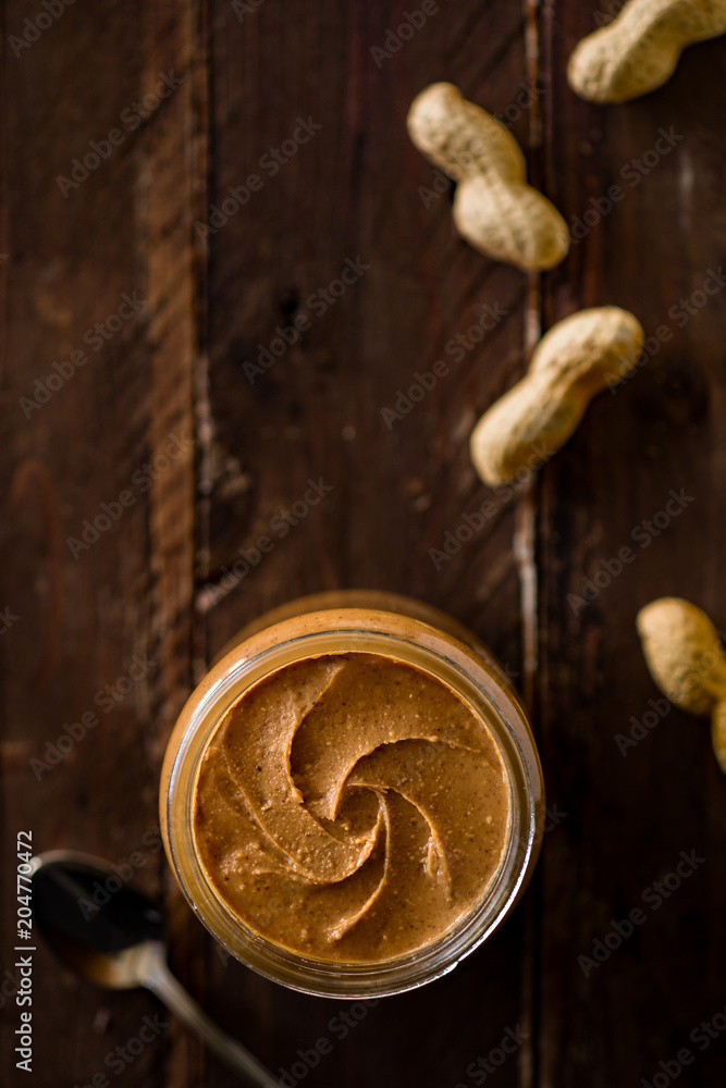 Fototapeta premium Peanut Butter in a Glass Jar with Peanuts on Wood