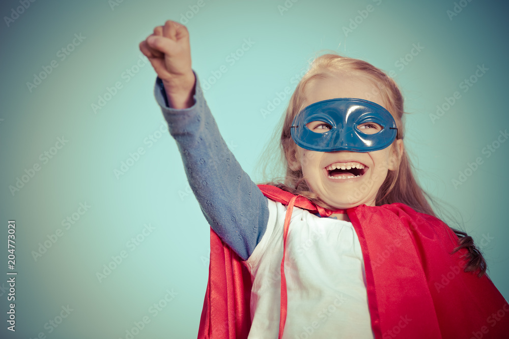 Funny little girl playing power super hero over blue sky background. Superhero concept. Funny little girl playing power super hero over blue sky background. Superhero concept.