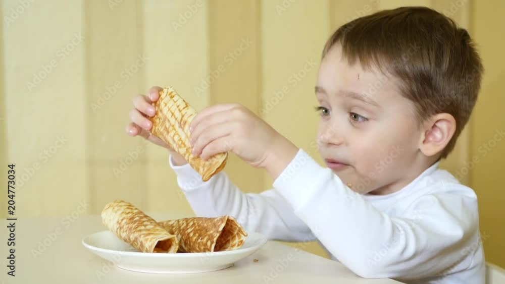 A happy child is eating wafer tubules while sitting at a table. A happy child is eating wafer tubules while sitting at a table.