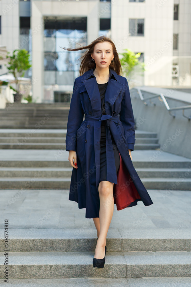 portrait of a woman walking in a coat on the background of the city and office center
