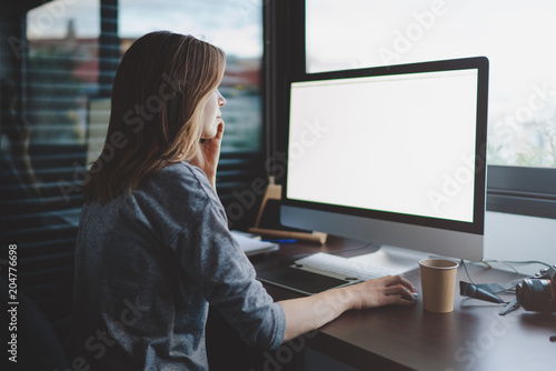 view from back to female student is talking on smartphone sitting at desk in front of monitor with blank space for design. Mockup screen with copy space. woman makes a business call photo