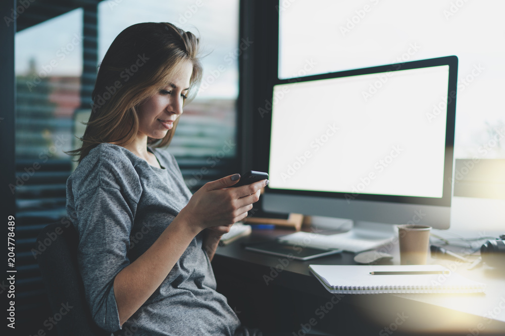 young female freelancer writing a text message on a modern mobile phone while sitting in the workplace in the home office. A modern business woman sends money by mobile bank. Mock up screen. young female freelancer writing a text message on a modern mobile phone while sitting in the workplace in the home office. A modern business woman sends money by mobile bank. Mock up screen.