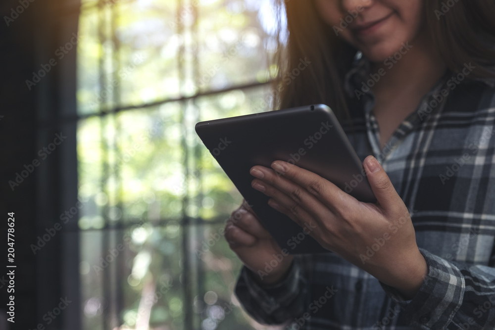Fototapeta premium A beautiful Asian woman with smiley face holding and using tablet pc in modern cafe