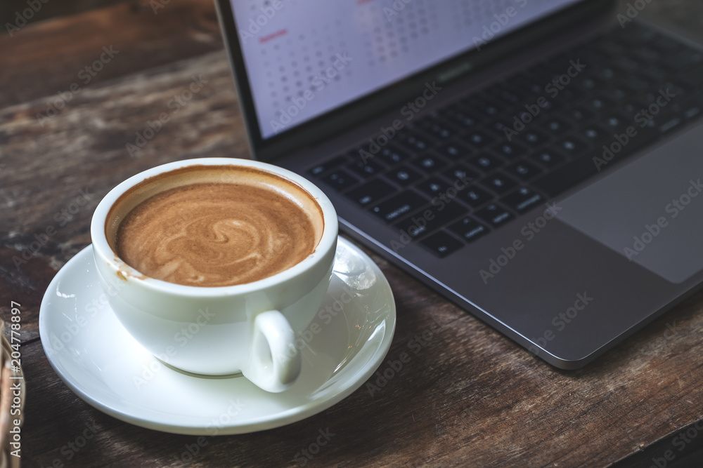 Closeup image of a cup of coffee and computer laptop on wooden table in cafe Closeup image of a cup of coffee and computer laptop on wooden table in cafe