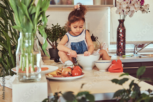 Sweet little cute girl learns to cook a meal in the kitchen.