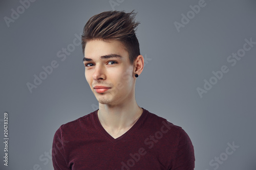 Handsome fashionable young guy with stylish hair and tattoo on his arm posing in a studio.