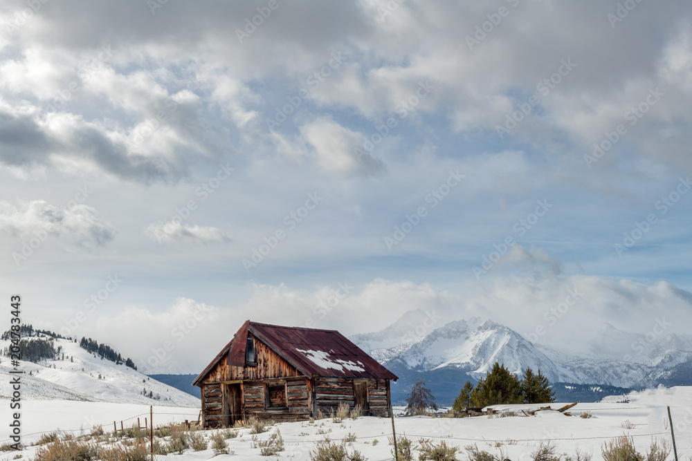 Rusted roofed log cabin in the Idaho wilderness winter with clouds in the sky