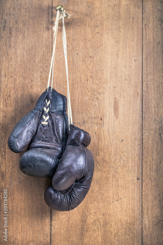 Pair of aged leather retro boxing gloves hanging on bronze nail front oak textured wooden wall background. Vintage style filtered photo © BrAt82
