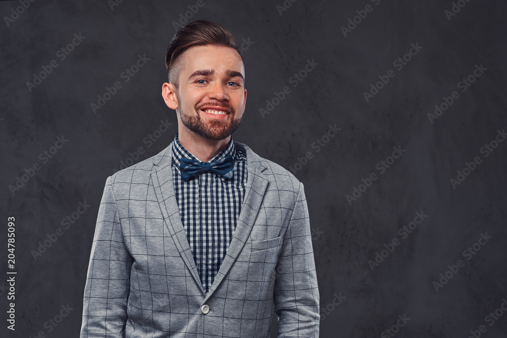 Smiling stylish bearded man with hairstyle in an elegant retro gray suit and bow tie, posing in a studio.
