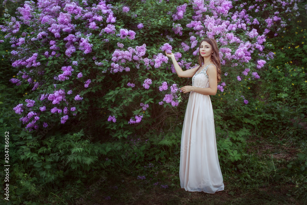 Young woman in a beautiful dress is standing near a lilac bush.
