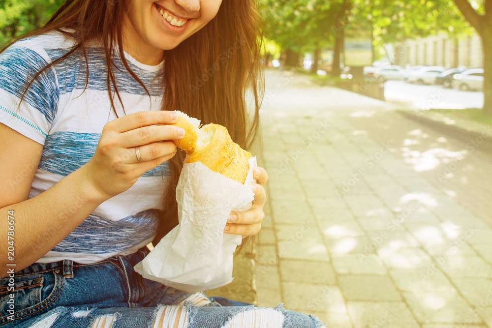 woman eating croissant on street. food to go