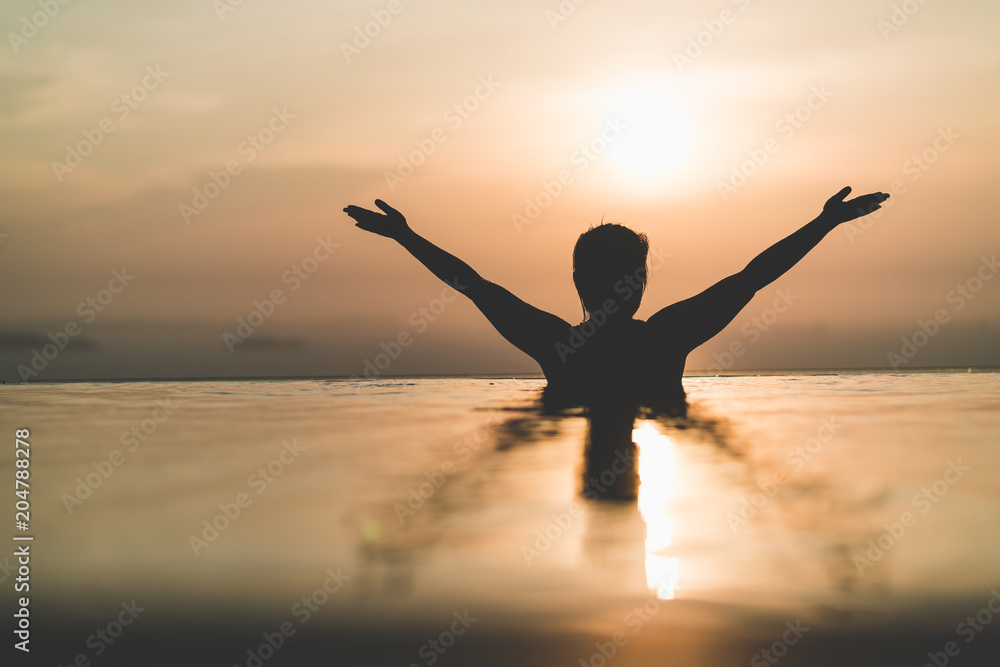 Black silhouette of asian woman splash water on summer vacation holiday relaxing in infinity swimming pool with blue sea sunset view. Healthy happiness lifestyle