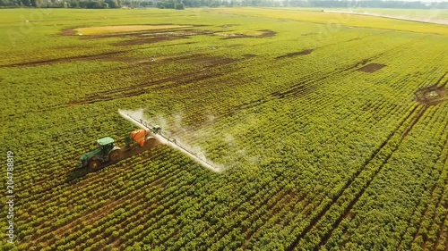 Aerial view tractor spraying the chemicals on the large green field. Spraying the herbicides on the farm land. Treatment of crops against weeds. 4K, aerial footage.