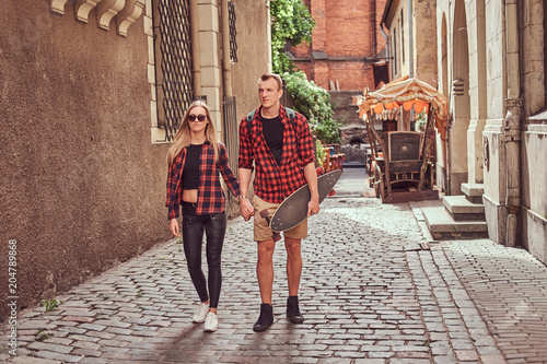 Young hipster couple, handsome skater and his girlfriend walking around an old narrow streets of Europe.