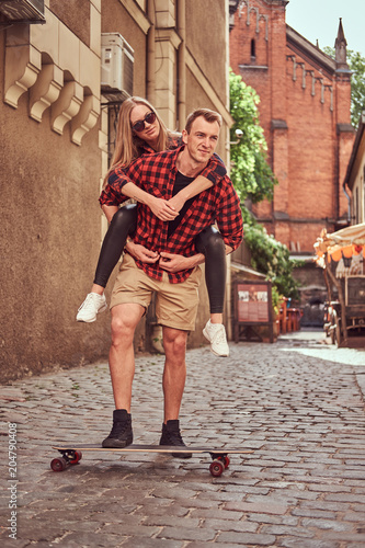 Young hipster couple, handsome skater and his girlfriend have fun while walking on the old narrow street of Europe.