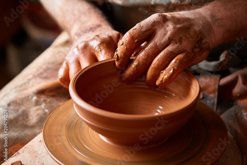 A potter paints a clay plate in a white in the workshop, top view, close-up, selective focus.