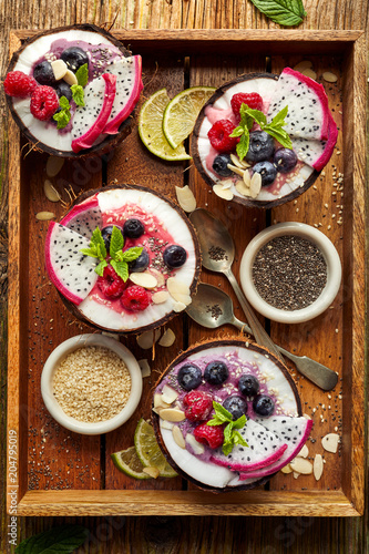 Berry smoothie in a coconut bowl with fresh Pitaya fruit (Dragon fruit), blueberries and raspberries, mint, almond flakes, chia seeds and sesame seeds. Healthy and delicious dessert or breakfast