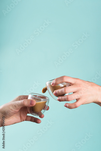 Closeup of men's and woman's hands clanging glasses with coffee together on pastel background