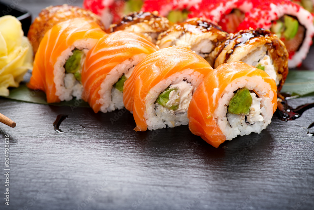 Sushi rolls closeup. Japanese food in restaurant. Roll with salmon, eel, vegetables and flying fish caviar on black slate background Sushi rolls closeup. Japanese food in restaurant. Roll with salmon, eel, vegetables and flying fish caviar on black slate background