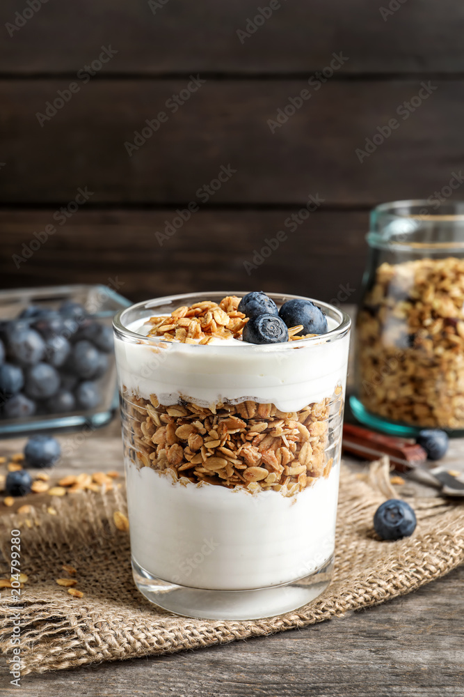 Glass with yogurt, berries and granola on wooden table Glass with yogurt, berries and granola on wooden table