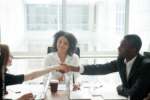 Smiling african businessman handshaking greeting caucasian businesswoman at group meeting negotiation, black satisfied entrepreneur welcoming partner shaking hand in lawyers office, respect concept