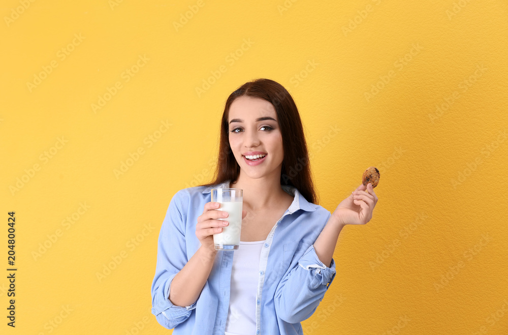 Beautiful young woman drinking milk with cookie on color background Beautiful young woman drinking milk with cookie on color background